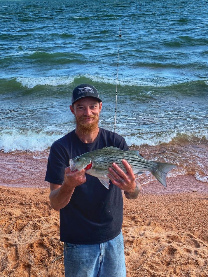 Image of guest and their bass catch on the beach at our Texas lake cabin rentals.