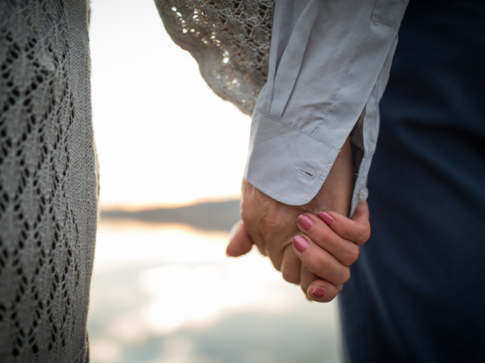 Image of couple holding hands walking by the lake shore.